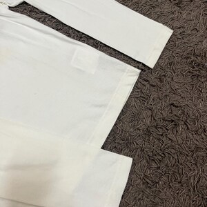 May include: A white long-sleeved shirt with a simple design. The shirt is made of a soft, likely cotton material. The sleeves and body of the shirt are visible, with a focus on the clean, minimalist aesthetic.