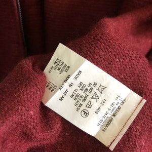 Puede incluir: Una etiqueta de cuidado blanca con texto negro y s&iacute;mbolos. La etiqueta est&aacute; unida a un su&eacute;ter burdeos. El texto en la etiqueta dice "MADE IN JAPAN", "QUALITY", "WASH", "DRY CLEAN", "COOL IRON", "DO NOT BLEACH", "DO NOT HAND WASH", "WOOL 55%", "ANGORA 17%", "NYLON 15%", "BEAVER 7%", "MINK HAIR 1%".