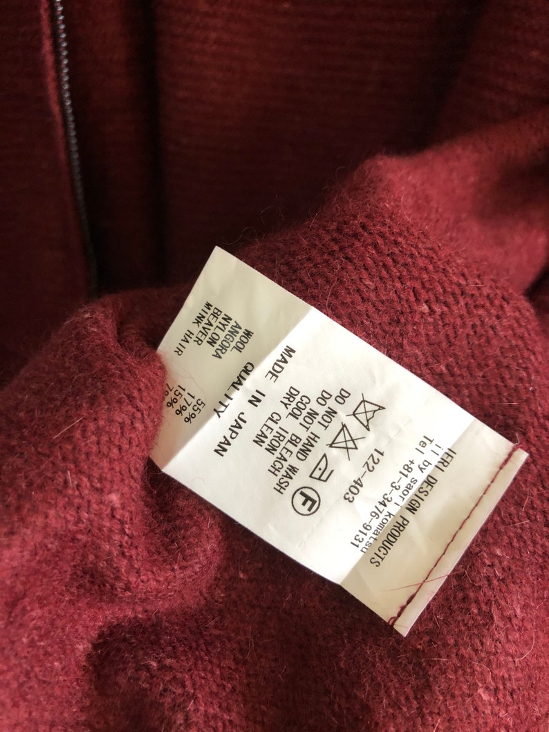 Puede incluir: Una etiqueta de cuidado blanca con texto negro y s&iacute;mbolos. La etiqueta est&aacute; unida a un su&eacute;ter burdeos. El texto en la etiqueta dice "MADE IN JAPAN", "QUALITY", "WASH", "DRY CLEAN", "COOL IRON", "DO NOT BLEACH", "DO NOT HAND WASH", "WOOL 55%", "ANGORA 17%", "NYLON 15%", "BEAVER 7%", "MINK HAIR 1%".
