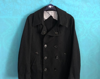 May include: A black double-breasted peacoat with four buttons. The coat is hanging on a hanger with a white and blue striped shirt underneath.