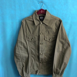 May include: A green denim jacket with a button closure and long sleeves. The jacket has a label on the left side of the chest that says "J.Crew".