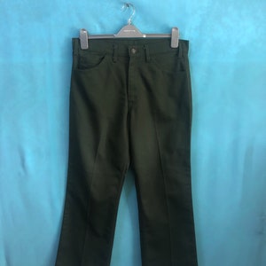 Op de afbeelding: Een donkergroene broek die aan een hanger hangt. De broek heeft een rechte pijp en een knoopsluiting.