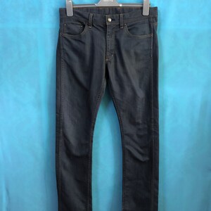 Peut inclure: Un jean en denim bleu foncé suspendu à un cintre noir sur un fond bleu clair.