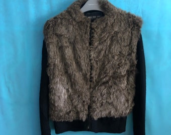 Puede incluir: Una chaqueta de piel sintética marrón con mangas de punto negro y cierre de cremallera. La chaqueta tiene una cintura de canalé negra y una etiqueta que dice "WORLD WIDE LOVE!"