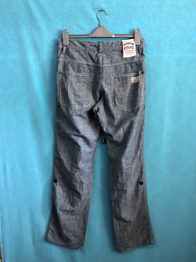 May include: Blue denim trousers with a green and white label that says "Elusion Uncomfortable Clothing".