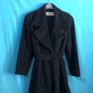 Puede incluir: Un abrigo de lana gris oscuro con cierre de doble botonadura y cinturón. El abrigo tiene cuello y mangas largas. La etiqueta "Karl Lagerfeld" es visible en el interior del abrigo.