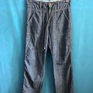 May include: A pair of blue denim trousers with a drawstring waist and a green and white cord. The trousers have two front pockets and two back pockets.