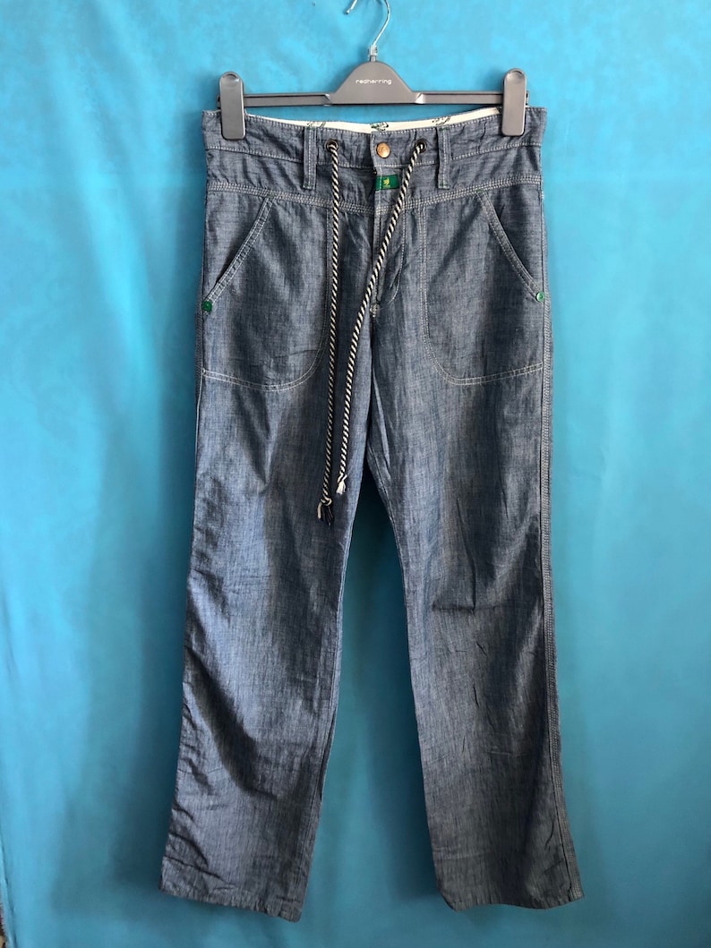 May include: A pair of blue denim trousers with a drawstring waist and a green and white cord. The trousers have two front pockets and two back pockets.
