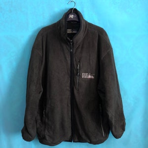 Pode incluir: Uma jaqueta de fleece cinza escuro com fecho de correr e dois bolsos com fecho de correr. A jaqueta tem o texto "FIRST DOWN" e um logotipo de montanha na frente.