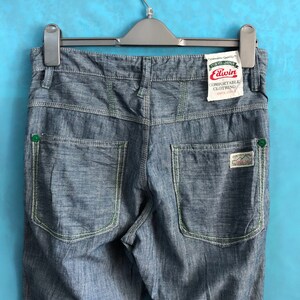 May include: Blue denim jeans with green stitching and a white label that says "Edwin Comfortable Clothing Since 1961" hanging on a black hanger.