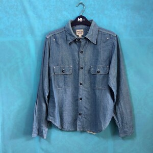 May include: A light blue denim long-sleeved shirt with a button-down collar, two chest pockets, and a button fastening. The shirt has a faded look and is hanging on a black hanger.