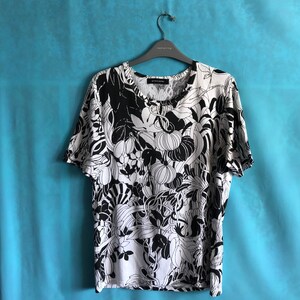 Könnte beinhalten: Ein weißes T-Shirt mit einem schwarz-weißen Blumendruck. Der Druck zeigt eine Vielzahl von Blumen und Blättern.