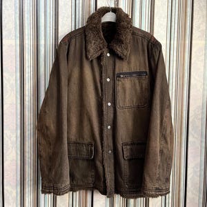 May include: A brown denim jacket with a faux fur collar and multiple pockets. The jacket has a button closure and a zippered pocket on the left chest.