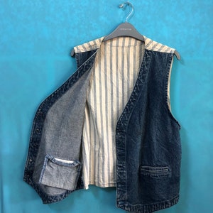 May include: A blue denim vest with a white striped lining. The vest has two pockets and a button closure.