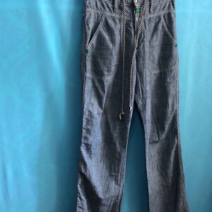 May include: A pair of blue denim trousers with a drawstring waist and two front pockets. The trousers have a subtle striped pattern and are hanging on a black hanger.