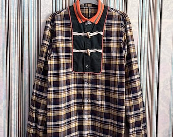 May include: A long-sleeved plaid shirt with a black, yellow, and brown plaid pattern. The shirt has a black corduroy panel with toggle closures and orange and green trim on the collar and cuffs. The shirt has the word "Stormhill" printed on the collar.