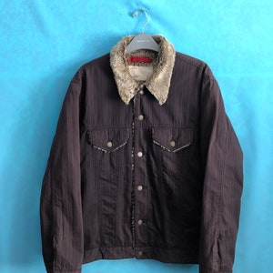 May include: A black denim jacket with a brown faux fur collar and striped pattern. The jacket has a button closure and two pockets.