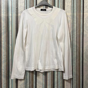 May include: White long-sleeve shirt with a large bow detail on the chest. The shirt has a crew neck and is hanging on a black hanger. The shirt is made of a soft, lightweight fabric.