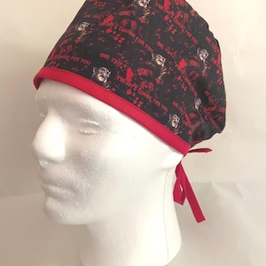 May include: Black surgical cap with a red trim and ties. The cap features a repeating pattern of a horror movie character and the text "ONE TWO FREDDY'S COMING FOR YOU" in red.