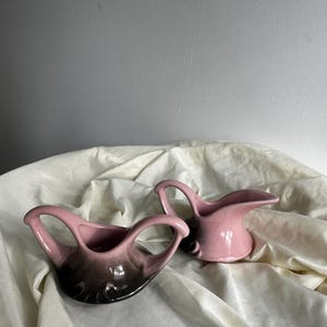 Peut inclure: Un ensemble de deux pots à crème et à sucre en céramique vintage. Les pots sont rose et noir avec un effet dégradé. Les pots ont une forme unique avec deux poignées.