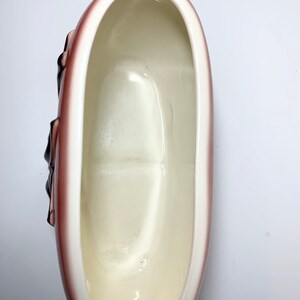 May include: A white ceramic planter shaped like a loaf of bread with a brown glaze. The planter has a smooth, glossy finish and is perfect for displaying small plants or flowers.