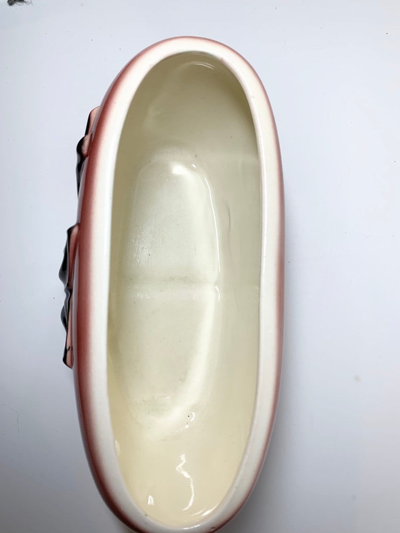 May include: A white ceramic planter shaped like a loaf of bread with a brown glaze. The planter has a smooth, glossy finish and is perfect for displaying small plants or flowers.