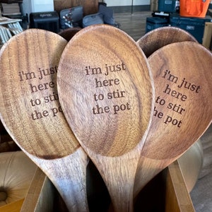 May include: Three wooden spoons with the text "i'm just here to stir the pot" engraved on them. The spoons are in a wooden container.