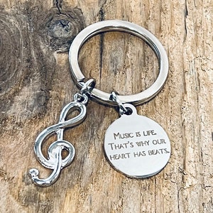 May include: Silver key chain with a treble clef charm and a round tag that reads "Music is life. That's why our heart has beats."
