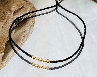 May include: A black string bracelet with two rows of gold beads.
