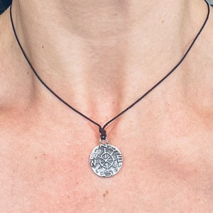 May include: A silver necklace with a compass pendant. The pendant is round and has a detailed design with the letters N, E, S, and W.
