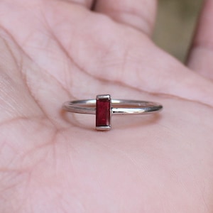 May include: A silver ring with a rectangular red gemstone.