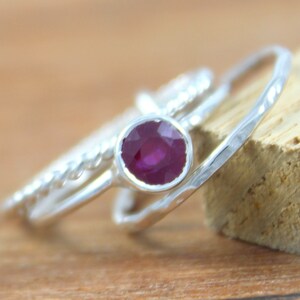 Peut inclure: Trois bagues en argent avec une pierre pr&eacute;cieuse rubis rouge fonc&eacute; dans la bague du milieu. Les bagues sont empil&eacute;es les unes sur les autres.