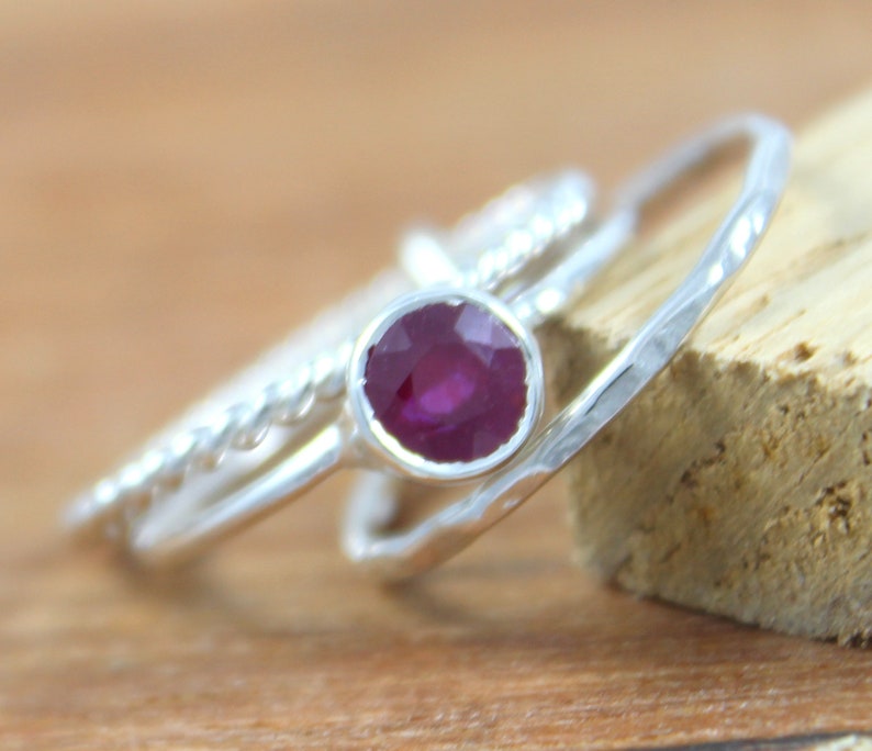 Peut inclure: Trois bagues en argent avec une pierre pr&eacute;cieuse rubis rouge fonc&eacute; dans la bague du milieu. Les bagues sont empil&eacute;es les unes sur les autres.