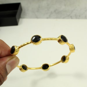 May include: Gold bangle bracelet with six black gemstones. The bracelet has a hammered texture.