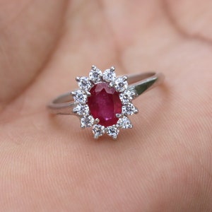 Puede incluir: Un anillo de plata con un gran rubí ovalado rodeado de diamantes más pequeños.