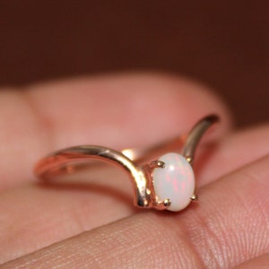 May include: A delicate rose gold ring with a white opal gemstone set in a V-shaped band.
