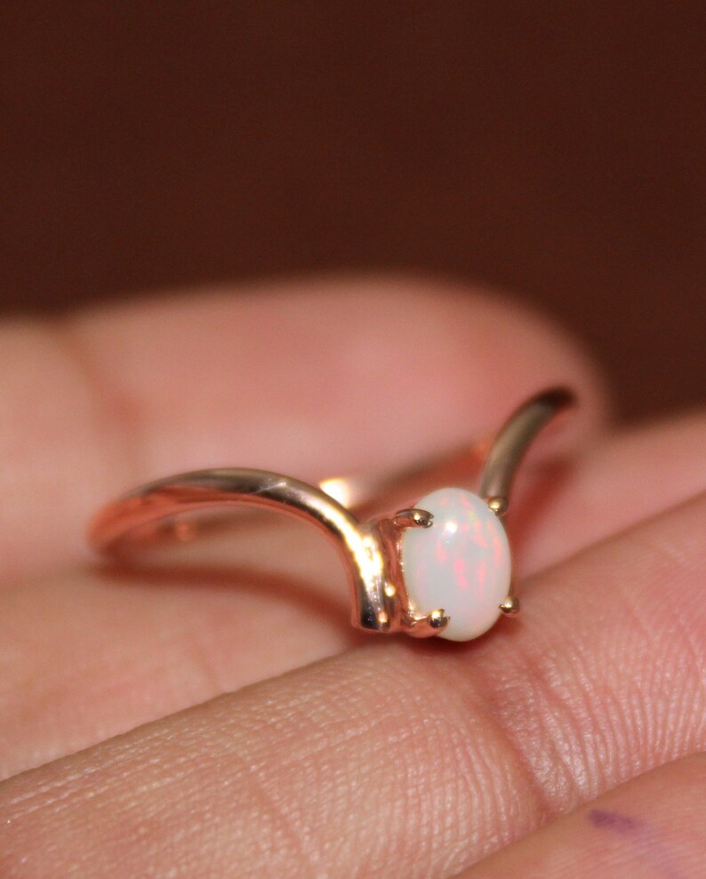 May include: A delicate rose gold ring with a white opal gemstone set in a V-shaped band.