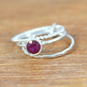 Peut inclure: Un ensemble de trois bagues en argent, dont une avec une pierre pr&eacute;cieuse en rubis rouge. Les bagues sont empil&eacute;es les unes sur les autres.