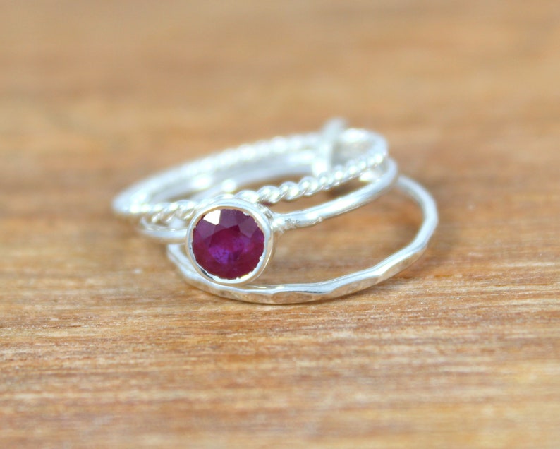 Peut inclure: Un ensemble de trois bagues en argent, dont une avec une pierre pr&eacute;cieuse en rubis rouge. Les bagues sont empil&eacute;es les unes sur les autres.