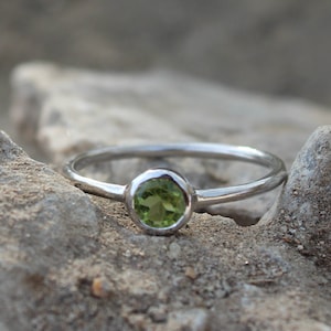 Pode incluir: Um anel de prata com uma gema oval verde. O anel está sobre uma rocha cinza e áspera.