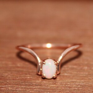 May include: A delicate rose gold ring with a white opal gemstone set in a simple, elegant design.