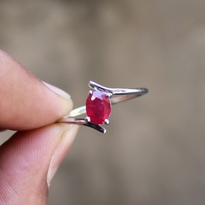 Puede incluir: Un anillo de plata con una piedra preciosa de rubí rojo. El anillo tiene un diseño simple y elegante con una banda curva.