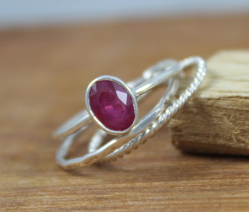 Puede incluir: Un anillo de plata con una gran gema de rub&iacute; de corte ovalado. El anillo tiene un engaste biselado y est&aacute; acompa&ntilde;ado de dos bandas de plata adicionales, una con un dise&ntilde;o de cuerda trenzada. El rub&iacute; es de color rojo intenso.