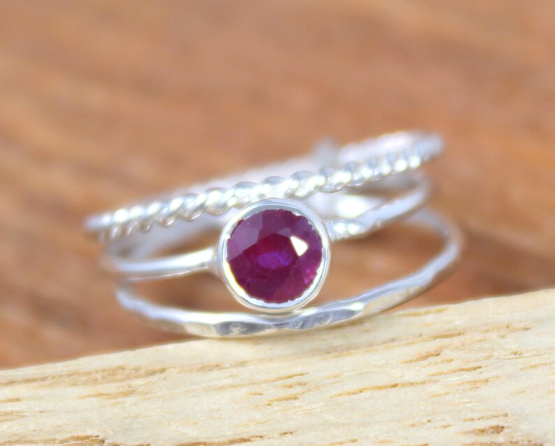 Peut inclure: Une bague en argent compos&eacute;e de trois anneaux, l'anneau sup&eacute;rieur pr&eacute;sente un motif de corde torsad&eacute;e, l'anneau du milieu est uni et l'anneau inf&eacute;rieur est martel&eacute;. Un seul rubis rond est serti au centre de la bague.