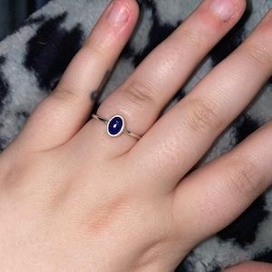Op de afbeelding: Een zilveren ring met een donkerblauwe ovale edelsteen.