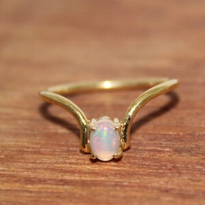 May include: A gold ring with a delicate, curved design features a white opal gemstone in the center.