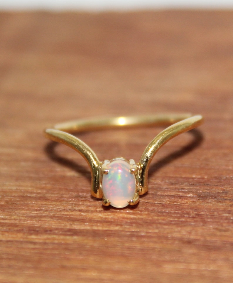 May include: A gold ring with a delicate, curved design features a white opal gemstone in the center.