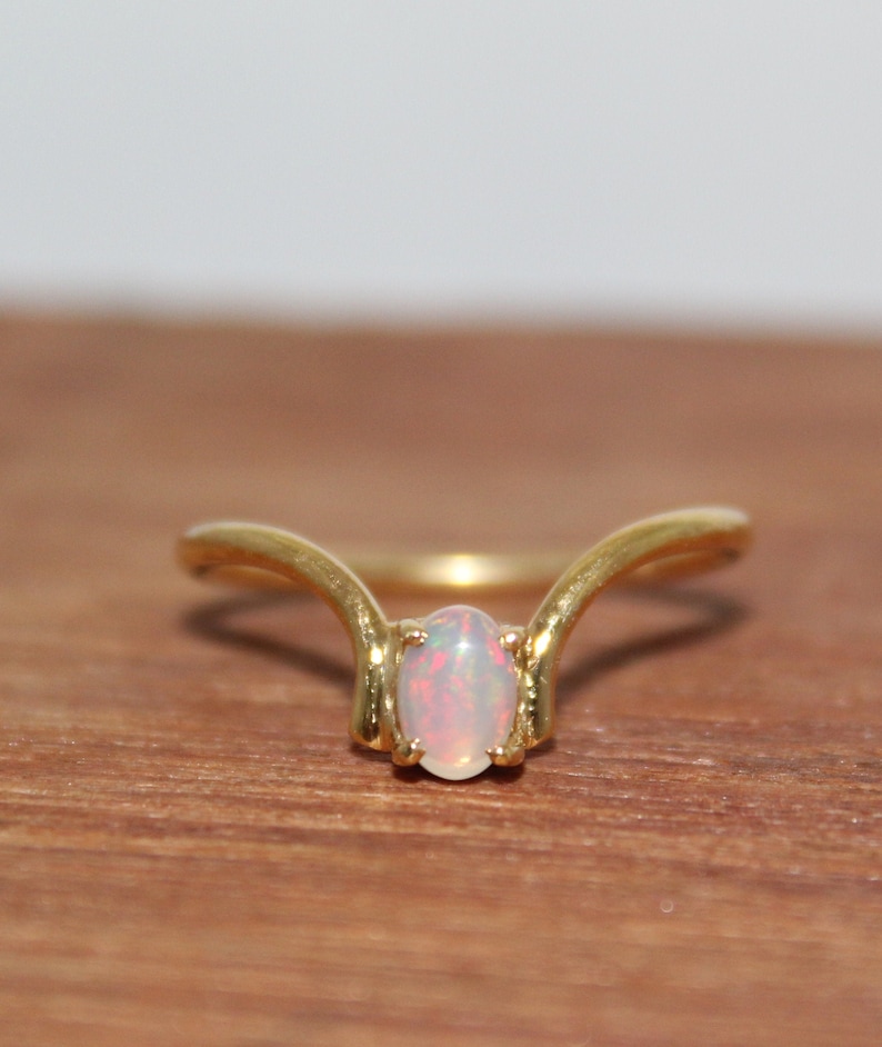 May include: A gold ring with a delicate, curved design features a white opal gemstone in the centre.
