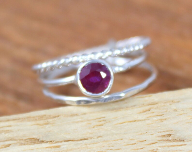 Peut inclure: Une bague en argent compos&eacute;e de trois anneaux, l'anneau sup&eacute;rieur pr&eacute;sente une petite pierre de rubis ronde de couleur rouge fonc&eacute;.