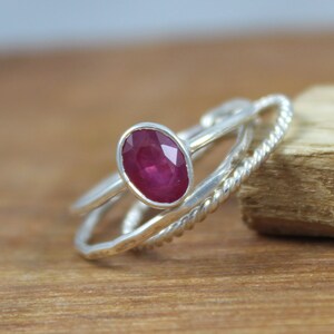 Puede incluir: Un conjunto de tres anillos de plata. El anillo principal presenta un rub&iacute; ovalado de color rojo intenso. Los otros dos anillos tienen dise&ntilde;os &uacute;nicos, uno con una textura de cuerda trenzada y otro con una banda lisa.